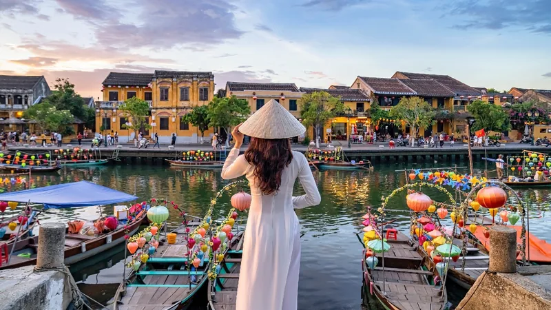Cô gái mặc áo dài trắng, đội nón lá ngắm những chiếc thuyền treo đèn lồng bên sông Hoài An lúc hoàng hôn.