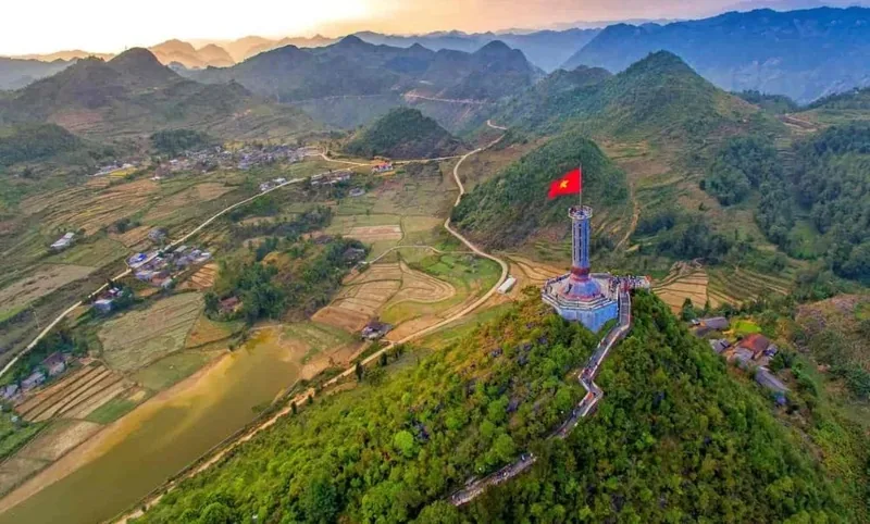 Cột cờ Lũng Cú với lá quốc kỳ Việt Nam trên đỉnh núi, nhìn xuống ruộng bậc thang và núi đá Hà Giang.