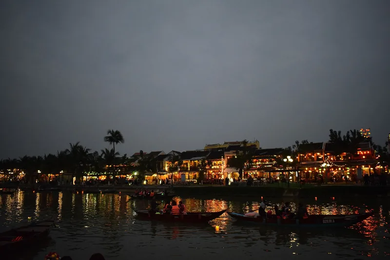 Những chiếc thuyền nhỏ chở du khách trên sông ngang qua các ngôi nhà rực sáng đèn ở Hội An lúc chập tối.