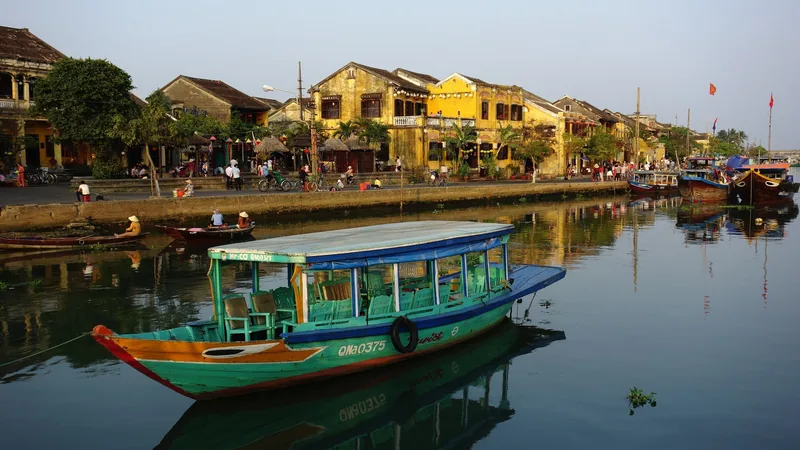 Một chiếc thuyền gỗ đầy màu sắc nổi trên sông trước dãy nhà cổ màu vàng ở phố cổ Hội An.