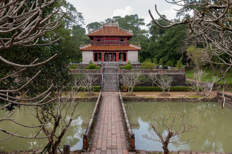 Lăng Minh Mạng ở Huế với đình mái đỏ được nối bằng cây cầu đá bắc qua hồ nước tĩnh lặng.