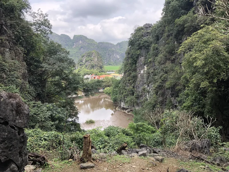 Những vách núi đá vôi bao quanh dòng sông đục và cánh đồng lúa, xa xa là ngôi làng ở Tam Cốc, Ninh Bình.