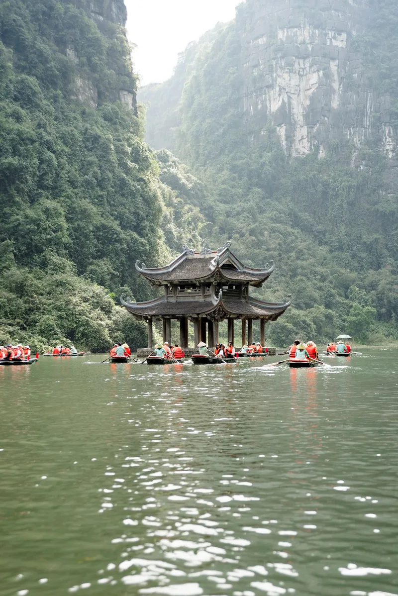 Thuyền chở du khách mặc áo phao đỏ đi qua đình gỗ giữa những núi đá vôi ở Tràng An, Ninh Bình.