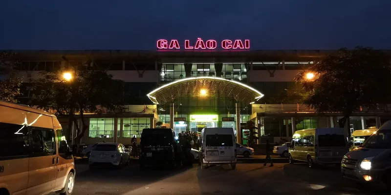 Ga Lào Cai sáng đèn ban đêm với biển hiệu neon và xe cộ đậu bên ngoài gần Sa Pa, Việt Nam.